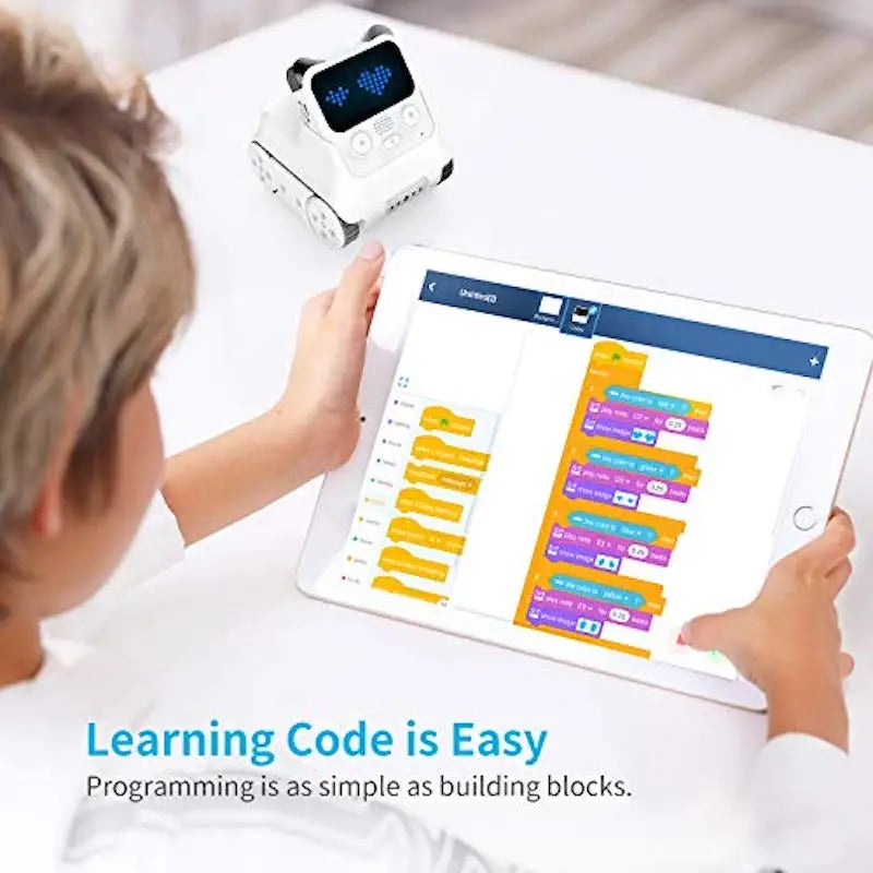 Child using a tablet with coding software and a small robot on a table.