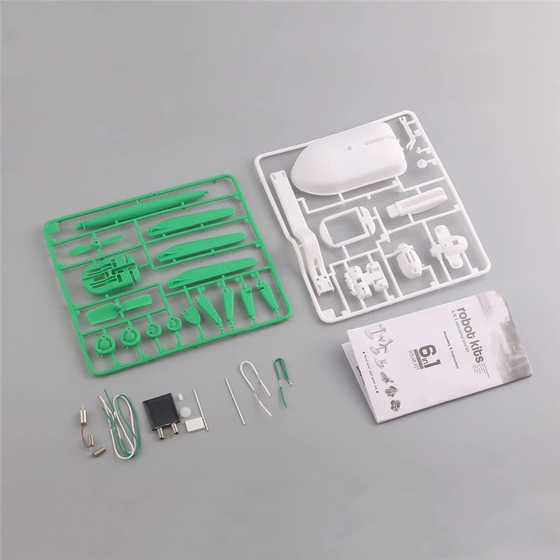 Robot kit components including green plastic parts, white electronic components, and a manual on a gray background